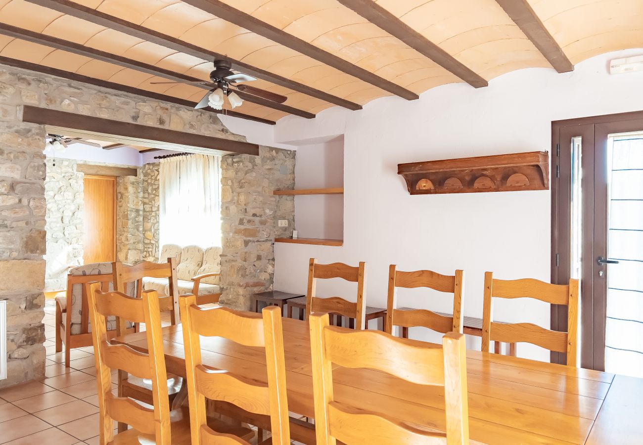 Spacious dining room in El Molí, a rural holiday home in La Garrotxa, Girona. Large wooden table, stone walls, and rustic wooden beams, perfect for fa