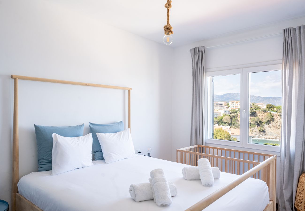 Dormitorio doble con estructura de madera, cuna y vistas al mar en un apartamento vacacional en Llançà, Costa Brava