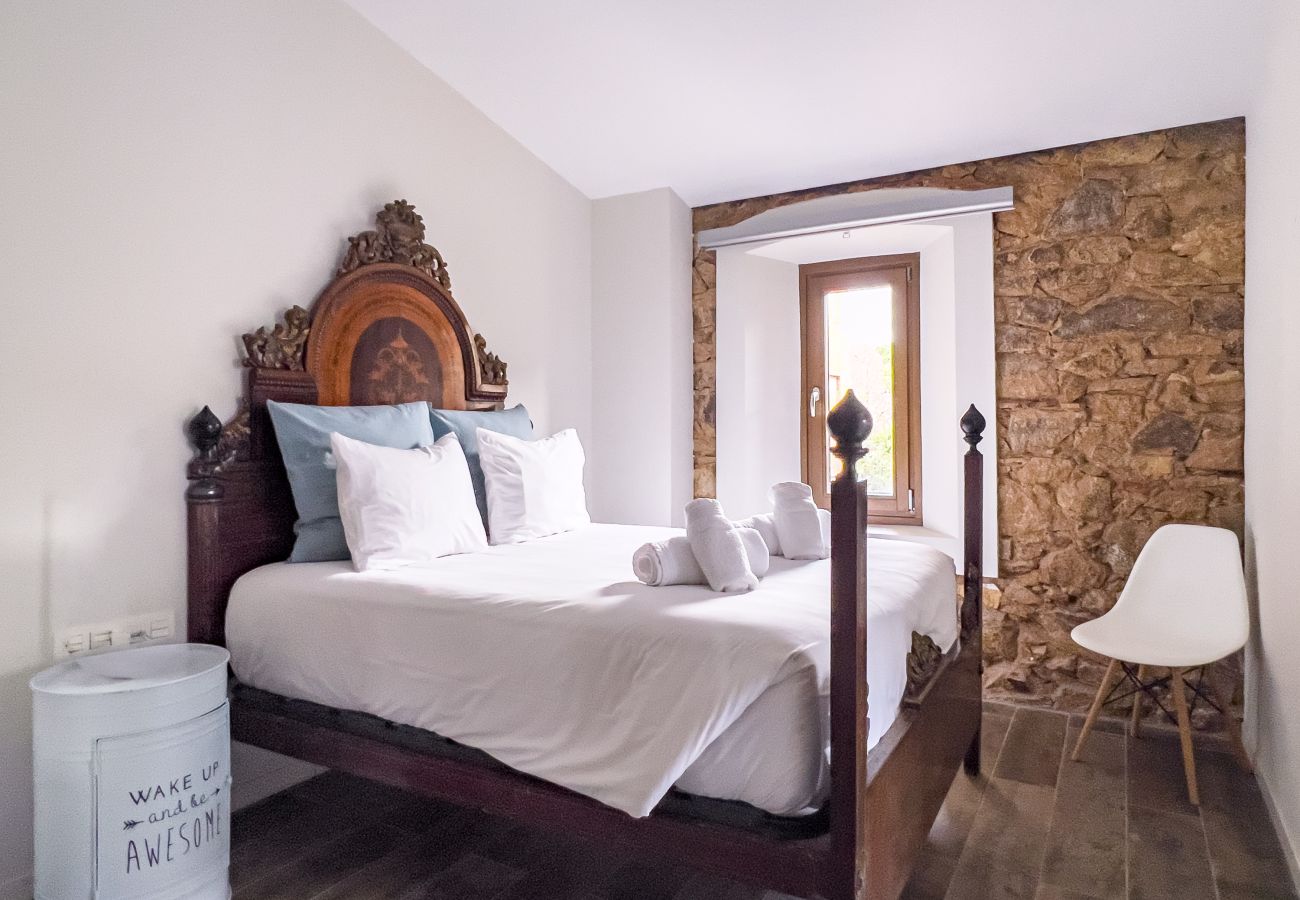 Dormitorio doble con cama de marco tallado y pared de piedra vista en un castillo de Girona