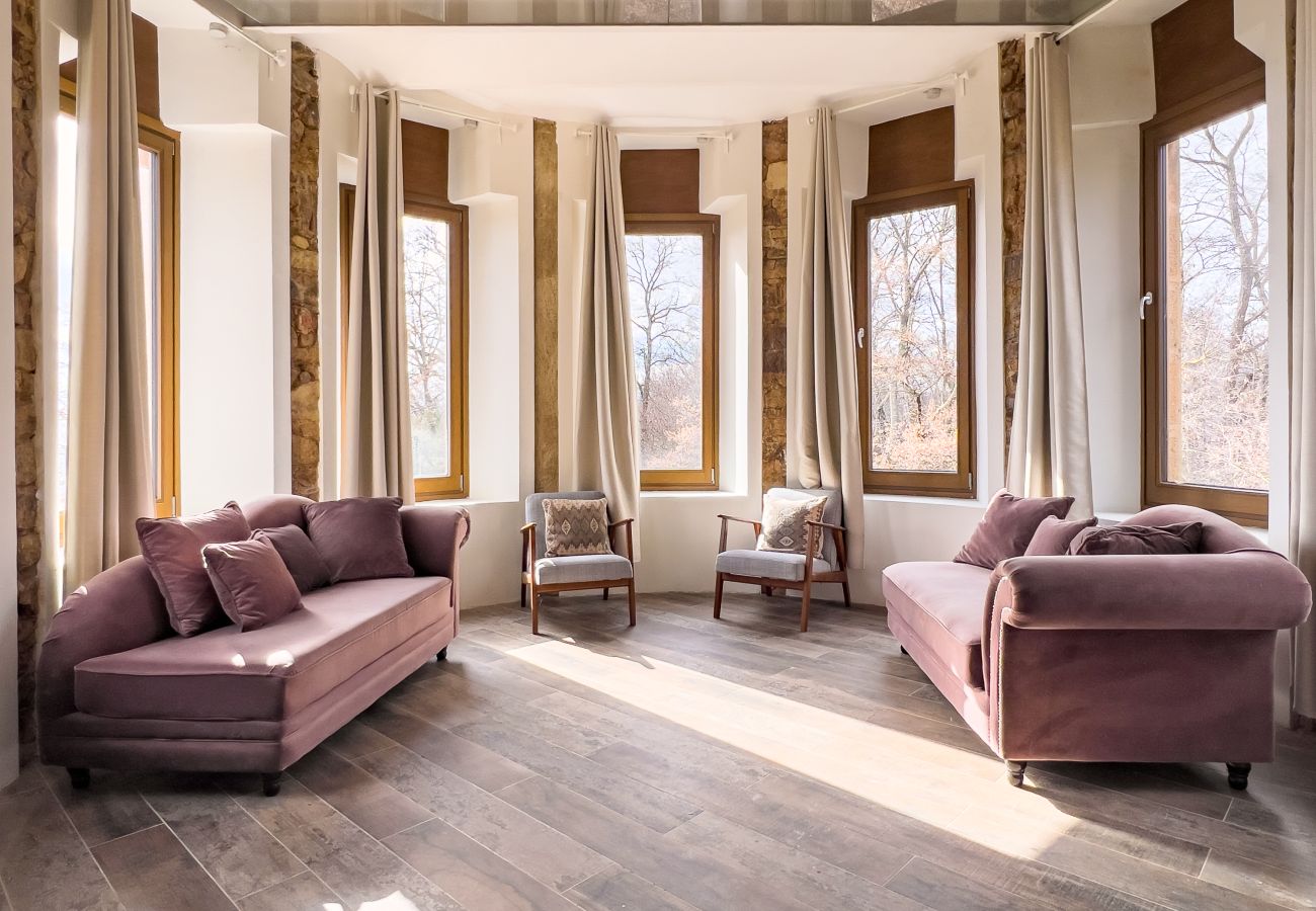Sala de estar circular en torre con techo de cristal, sofás de terciopelo y vistas al bosque en un castillo de Girona