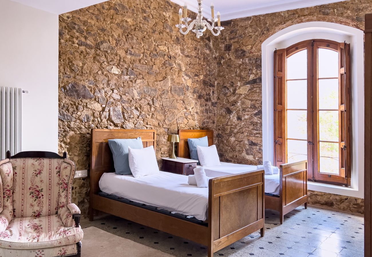 Dormitorio twin con pared de piedra vista y vistas al jardín de la capilla en un castillo de Girona