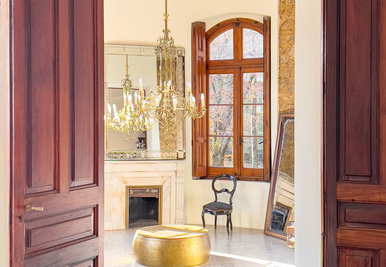 Sala circular en torre con araña de latón, chimenea decorativa de piedra y ventana arqueada en un castillo de Girona